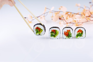 Sushi with sakura twig and chopsticks on a light background. Female hand takes sushi with chopsticks