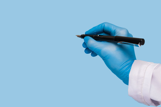 A Female Hand In A Medical Glove And In A White Coat Holds A Pen And Writes In The Air On A Blue Background. Mock Up