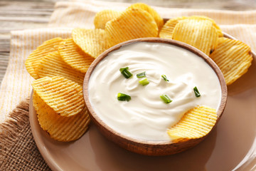 Tasty sour cream and potato chips on table