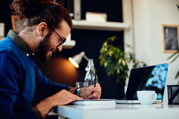 Young innovative dedicated bearded employee sitting in his home modern office and drawing. Work from home concept.
