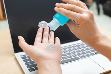 close up hand using sanitizer gel for hand hygiene coronavirus prevention before work with laptop at home.