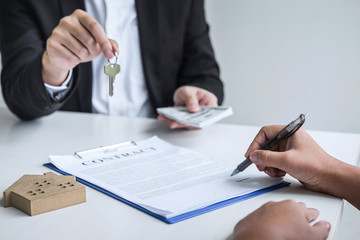 Estate agent giving house keys to client after signing agreement contract real estate with approved mortgage application form, concerning mortgage loan offer for and house insurance