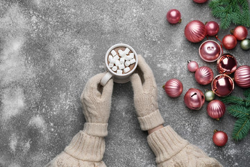 Female hands with cup of hot chocolate and Christmas balls on grey background