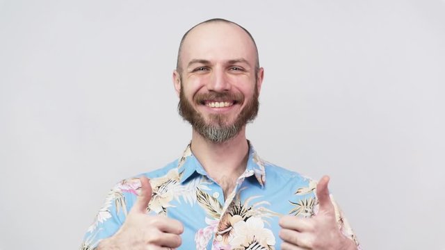 Happy bearded man wearing hawaiian shirt showing thumbs up over white background. Good job, very well. Slow Motion.