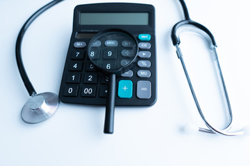 Concept of medical expenses or medical insurance for blog title and header. Stethoscope,white calculator and magnifying glass on wooden background.