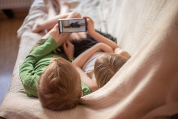 kids play telephen, watch videos on gadgets lying on the couch