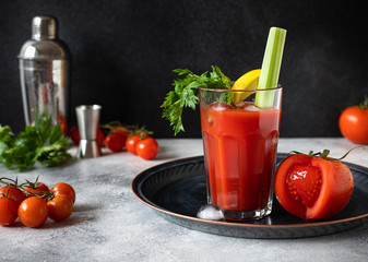 Classic alcoholic cocktail Bloody Mary with ice, lemon and celery. Cocktail ingredients and bar tools on a gray table and black background