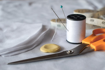 Needle and pin on white thread rolls for hand sewing on white cloth with tape measure and sketch yellow chalk with scissors cut on the fabric close-up.