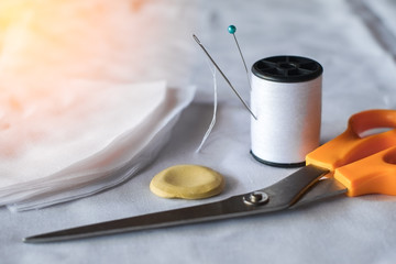 Needle and pin on white thread rolls for hand sewing on white cloth with tape measure and sketch yellow chalk with scissors cut on the fabric orange light close-up.