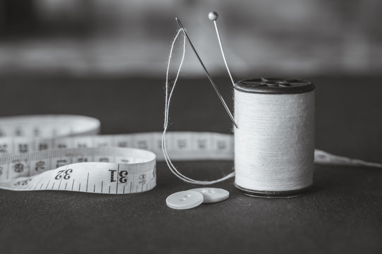 Needle and pin on white thread rolls for hand sewing on white cloth with tape measure and clasper on the fabric black and white tone (monochrome) close-up.