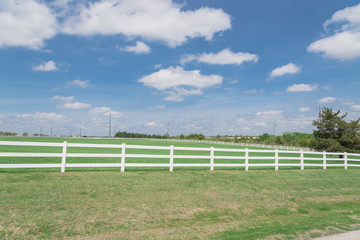 Long wooden white fence to horizontal line in cloud blue sky at farmland in Ennis, Texas, USA