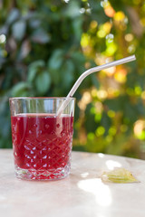 a glass with a tasty and aromatic drink with a reusable metal straw on a table against a background of greenery in the sun