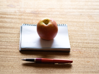Apple on a notepad and a pen on a wooden table.
Concept: health and intelligence