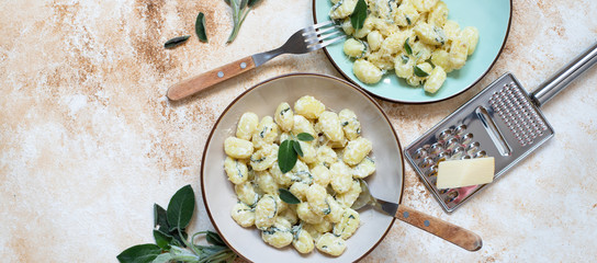 Italian homemade gnocchi with butter, cheese and sage served in two plates on a light marble table. Italian food. Copy space. Banner. Flat lay - obrazy, fototapety, plakaty