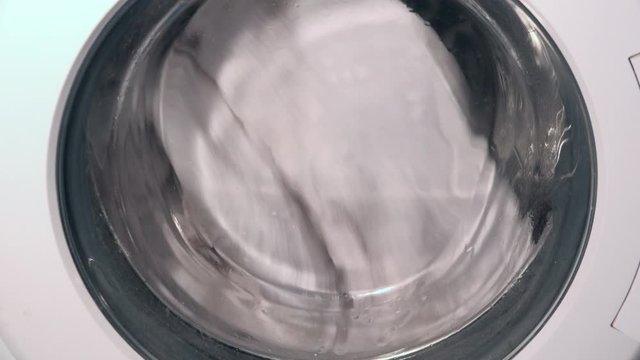 Clothes turning around in washing machine close up 4K