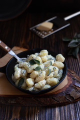 Italian homemade gnocchi with butter and sage served in a pan on a wooden cutting board. Italian food. Wooden table. Dark background. Copy space. Vertical