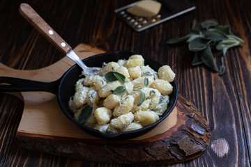 Italian homemade gnocchi with butter and sage served in a pan on a wooden cutting board. Italian food. Wooden table. Dark background. Copy space