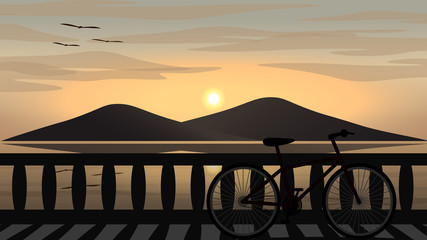 A bicycle is parking on a coast road with sea and an island at sunset.