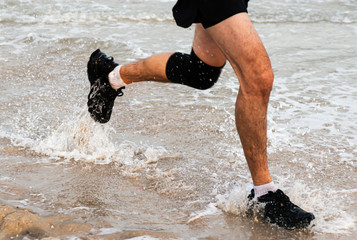Runner running in water wearing sneakers and knee brace at thebeach on the waters edge