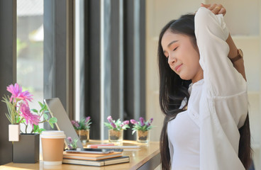 Asian women sit in the workspace and stretch their arms to relax during an online meeting with a laptop.