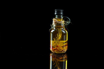 Bottle of olive oil with spices and rosemary on a black background.
