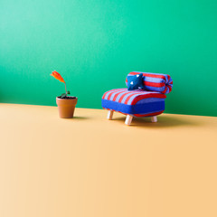 Blue red chair toy sofa and blooming red lower bud flowerpot. Green wall, yellow floor background. Copy space. Minimalist concept