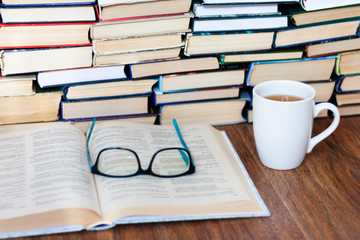 Open textbook, glasses, cup of tea and stack of old book on wooden table, education concept background, many books piles with copy space for text.