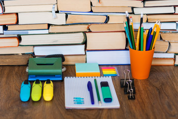 School stationery accessories - notebook, copybook stack with plastic holder pencils, pens, markers, paper clips, stickers, notepads, sharpener with stack of books education concept background.