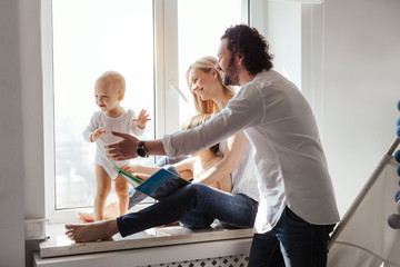 Happy smiling modern caucasian family playing and spending time in a bright white room near the window. Sunny day. Perfect parenting relationship. Parents of two cute boys.
