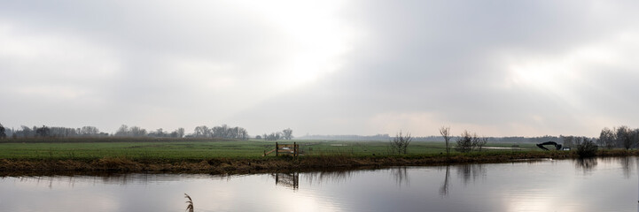 Cloud overcast sky with rays of sunshine over a grassland and a river or canal in the rural area near Amsterdam Netherlands