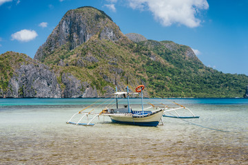 Fototapeta na wymiar Palawan island, Philippines. Low angle view of traditional filippino boat in shallow water in El Nido bay. Epic Cadlao island in background