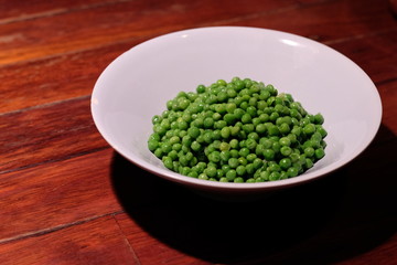 close up a bowl of cooked green soya bean on wooden table. blur background