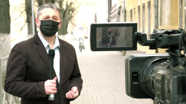 A middle- aged European journalist in a protective medical mask is reporting in a deserted city.