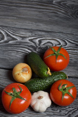 Tomatoes with green ponytails, onion and garlic head. Two green prickly cucumbers with yellow flowers. They lie on the surface of brushed pine boards.