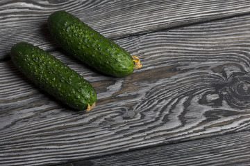 Two green prickly cucumbers with yellow flowers. They lie on the surface of brushed pine boards.