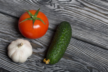 Tomato with a green ponytail, cucumber and garlic. They lie on the surface of brushed pine boards.