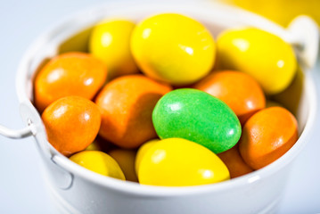 Small bucket full of yellow, orange and green round candies.