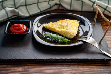 piece of omelet on black plate with ketchup.