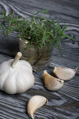 Head of garlic, a few cloves of garlic. A glass with rosemary branches. They lie on the surface of brushed pine boards.