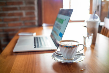 Hot aroma cappuccino coffee cup on wooden table work from home with laptop