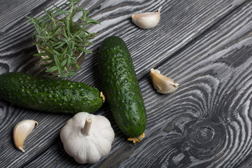 Spiky cucumbers, garlic and a glass with rosemary. On the surface of brushed pine boards.