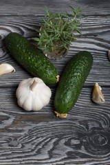 Spiky cucumbers, garlic and a glass with rosemary. On the surface of brushed pine boards.