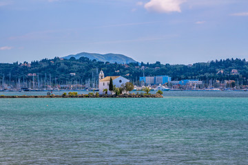 View of beautiful Gouvia Bay, ancient Ypapanti church – small white house on a pier, port marina, coast and mountains, covered with green trees. Summer landscape, Corfu Island, Greece. 