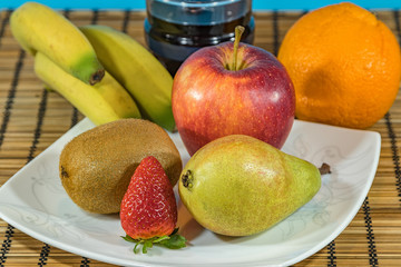 Fresh tropical and subtropical fruits in a large white dish. Glass of red wine on Wicker bamboo stand on the dining table. Close up, Selective focus