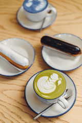 Blue and green matcha in glasses on a wooden table in a coffee shop next to a sweet dessert. Eclairs with chocolate ganache and icing with different toppings