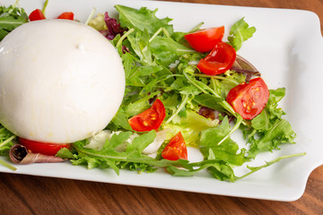 close up of burrata with salad on a wooden background