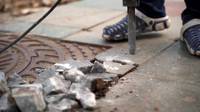 A jackhammer worker smashes a marble slab around an iron hatch