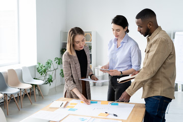 Busy young interracial colleagues discussing creative ideas for startup project while making task board