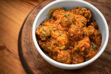Potato curry (Kashmiri dum aloo) served in bowl on wooden dining table.