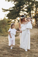 Happy elegant mother and her two beautiful daughters with flower wreaths in a nature at sunset